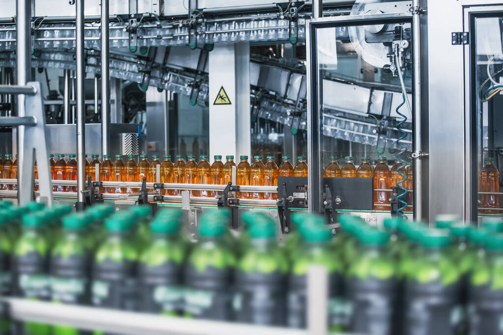 裝有新鮮有機果汁的塑料瓶，位于飲料廠或工廠內部的自動傳送帶或生產線上，配有現代工業機械設備